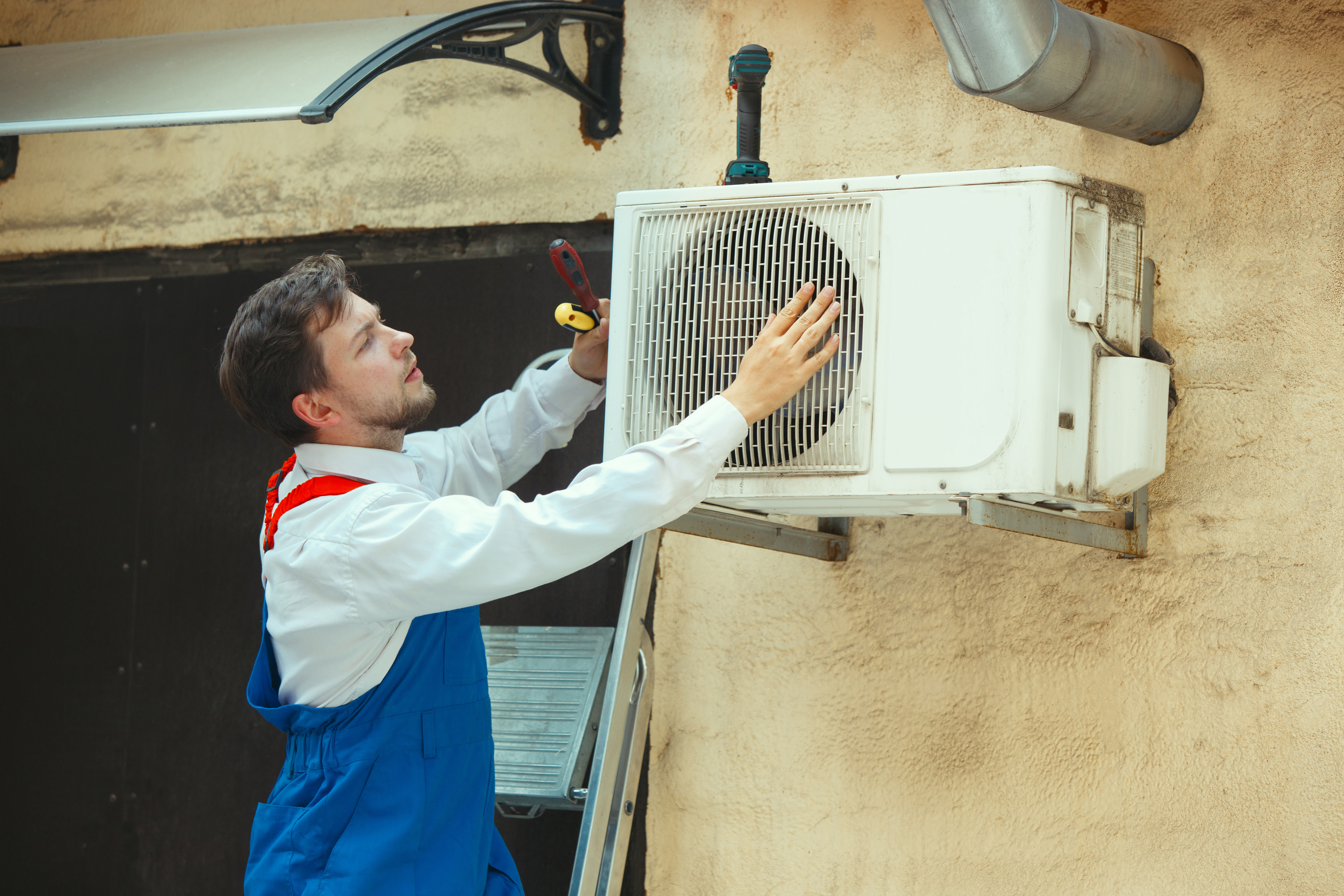 HVAC technician working on a capacitor part for condensing unit. Male worker or repairman in uniform repairing and adjusting conditioning system, diagnosting and looking for technical issues.